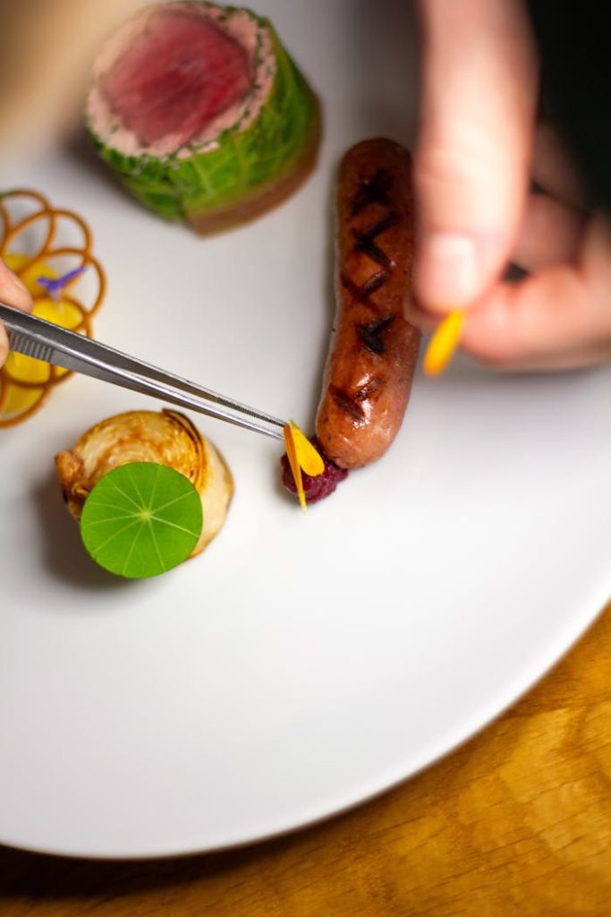 Close-up of a chef precisely plating a gourmet dish with sausage and vegetables.
