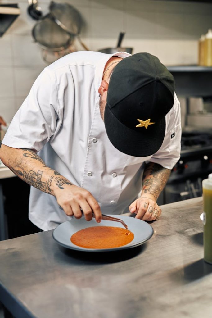 Chef in kitchen carefully presenting an elegant gourmet dish. Culinary artistry in action.
