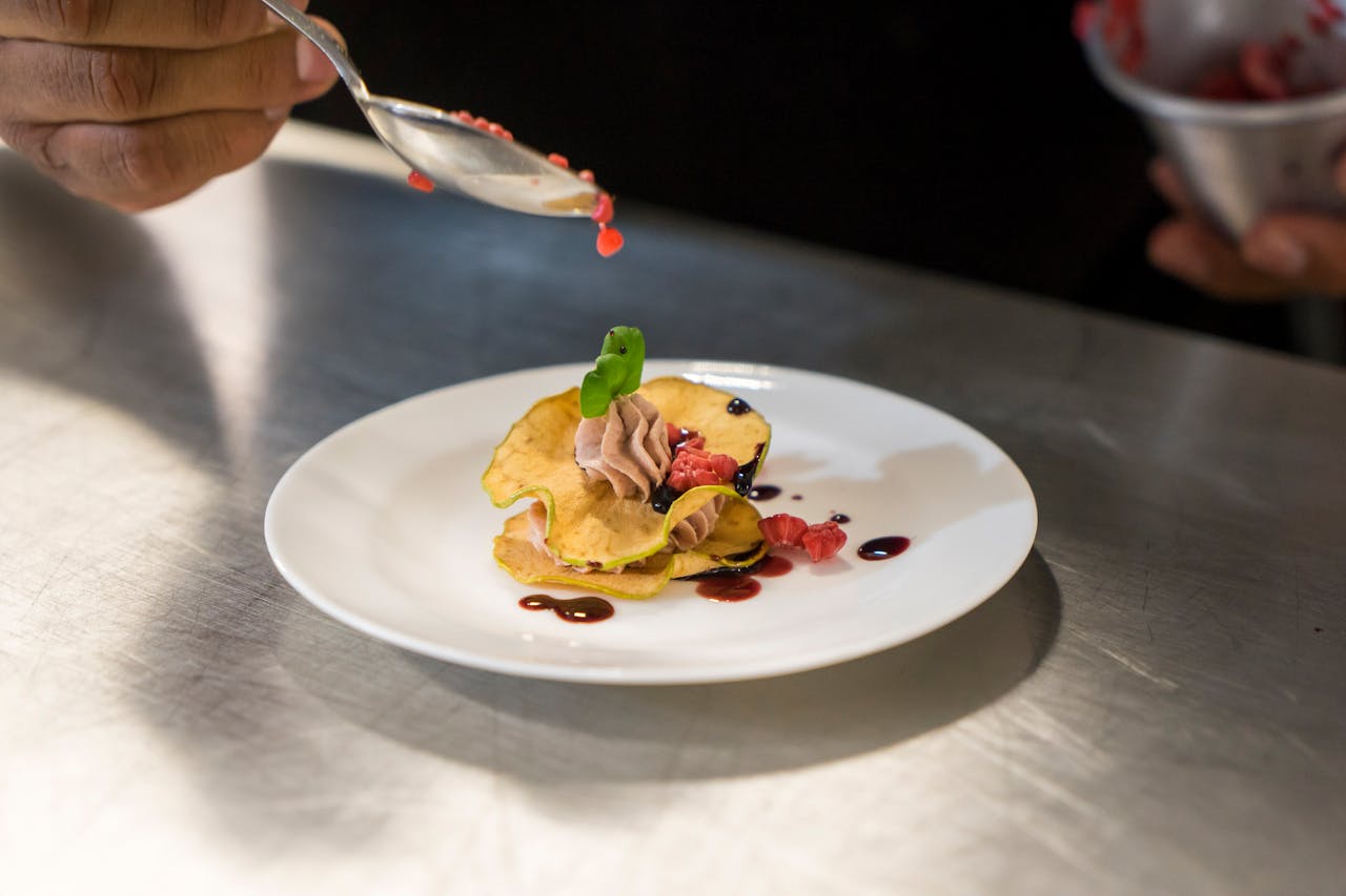 Close-up of a chef garnishing an elegant dessert with berry sauce on a white plate.