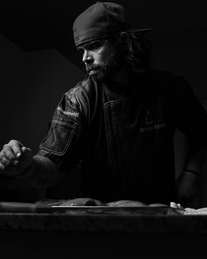 Black and white photo of a focused chef preparing food, captured in dramatic lighting.